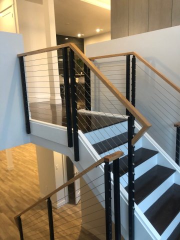 A picture of custom stair with dark steps and iron cables below handrails